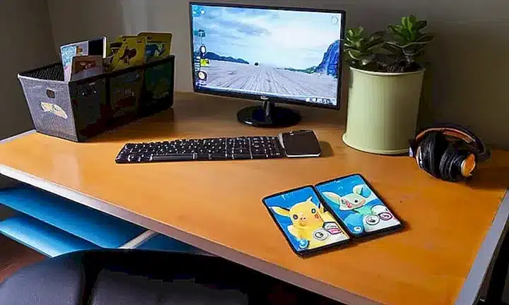 Un espacio de trabajo acogedor iluminado solo por una lámpara sobre un escritorio donde alguien juega al Pokémon Go en su PC y Switch