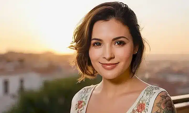 Una mujer con cabello oscuro se encuentra de pie en una colina soleada que mira hacia un pueblo al amanecer