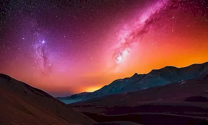 La imagen muestra una nebulosa majestuosa y brillante en el atardecer con colores vibrantes y un fondo naranja amarillento