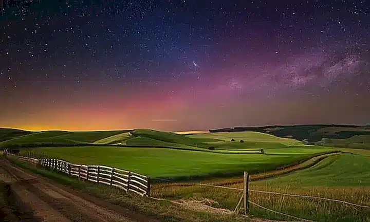 La campaña bajo un cielo estrellado ondea con constelaciones y una aurora borealis bailando sobre la distancia
