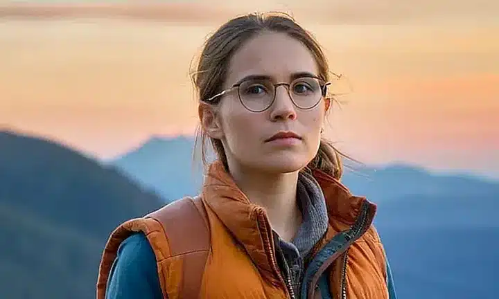 Un hombre está parado en una cima de montaña al atardecer, rodeado por un paisaje montañoso y pintoresco