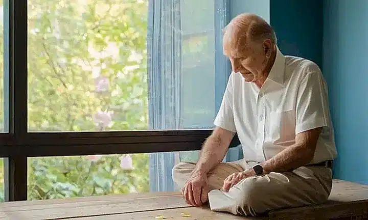 Un anciano sentado en una habitación tranquila acompañado de una vasija con rosas y un retrato del presidente Nelson detrás suyo, rodeados por la luz suave y el silencio