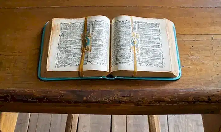 Una niña pequeña sostiene una Biblia en un escritorio de madera gastada, bañado por la luz tempranal que crea sombras claras y suave