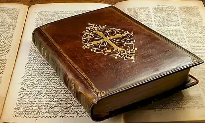 Una Biblia vieja y gastada descansa sobre un escritorio, iluminada débilmente por la luz matutina que filtra a través de la ventana