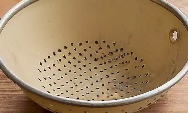 En la parte posterior de un colador en una mesa hay un fondo de canvas desgastado con pequeño deterioro y manchas de herrumbre