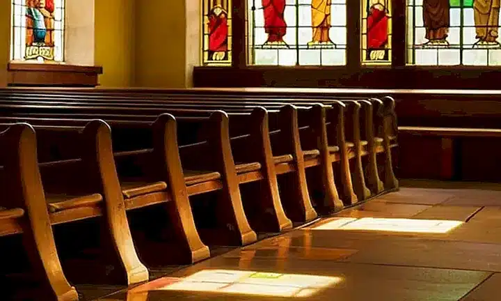En la iglesia, una púa de madera adornada con detalles artísticas proyecta sombras largas hacia una ventana de vidrio estuco a través de la cual se filtra una luz suave y cálida