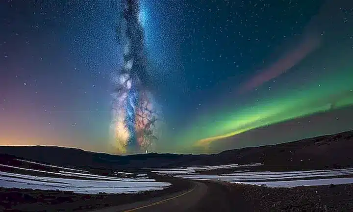 El cielo nocturno muestra una mezcla de colores con nubes y objetos celestes iluminados bañando el espacio