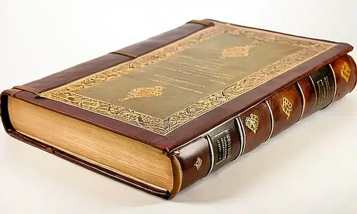 Una biblia antigua con cubierta de cuero marrón y detalles en filigreé dorado, con signos de desgaste y deterioro