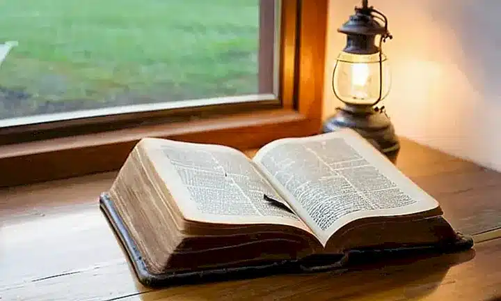 Un libro de biblia antiguo y bien cuidado está abierto sobre una mesa escritorio con luces suaves que iluminan las páginas dañadas