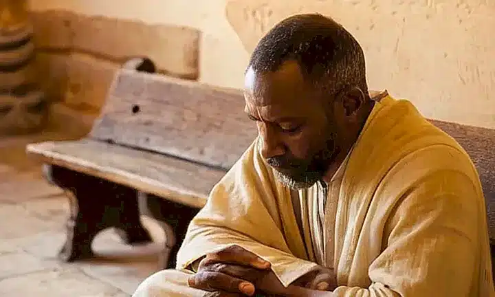 Un anciano con piel oscura se sienta en una bancada de madera, contemplando su Biblia, desgastado por el uso y la edad