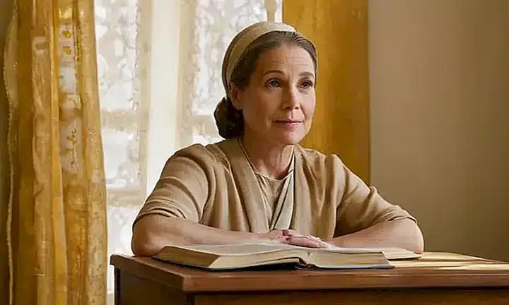 Una mujer religiosa anciana estudia su Biblia rodeada de libros antiguos bajo la débil luz del atardecer