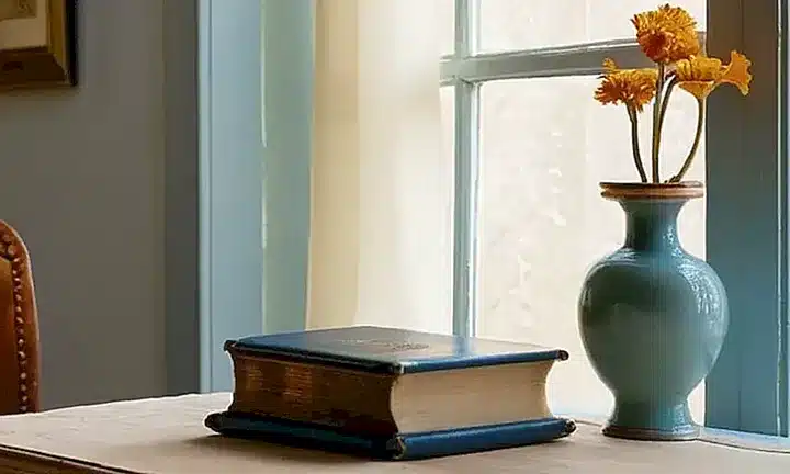 Una habitación tranquila llena de texturas y luces suaves destaca un escritorio antiguo y un libro abierto con una pluma de plata al lado