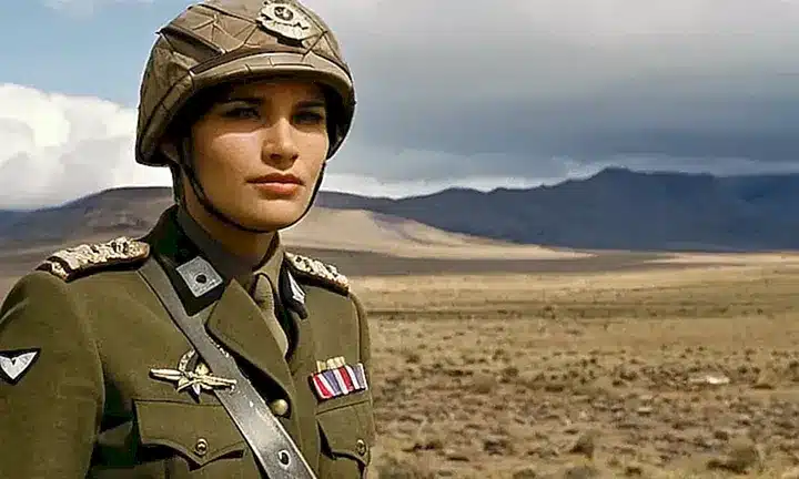 Un comandante está de pie en la distancia, con una vista deslumbrante detrás suyo, vistiendo uniforme militar y portando un bastón