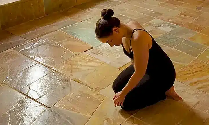 La fotografía muestra a una joven mujer en oración, rodeada de luces tiernas y arcos de vidrio colorido en un lugar histórico con texturas naturales