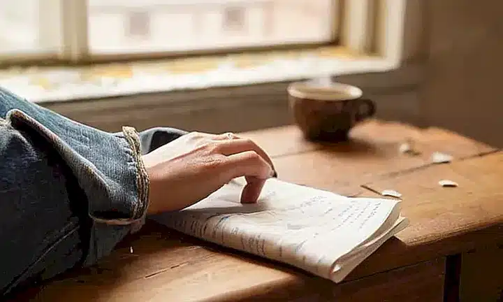 Una persona fatigada sentada en un escritorio antiguo, rodeada de notas y rodeado de oscuridad