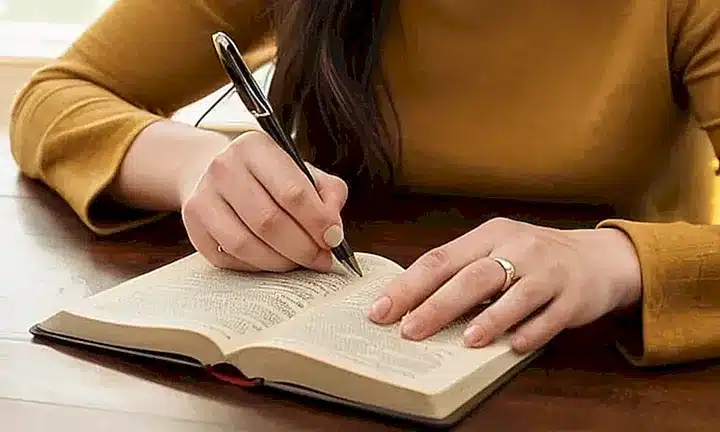 Una mujer anciana sentada frente a una mesa, con la Biblia y un bolígrafo en sus manos