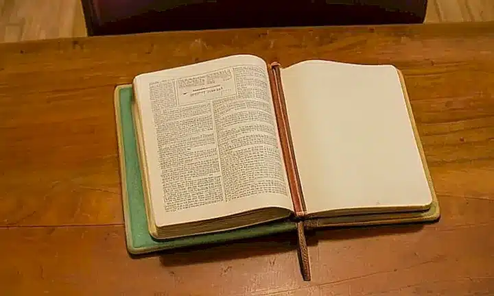 En un escritorio antiguo hay una Biblia abierta, rodeada de notas y lápices, bajo la luz cálida de una vela