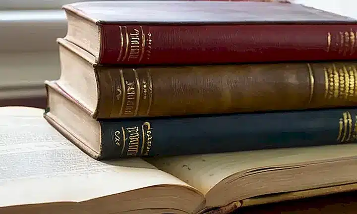 La Biblia desgastada descansa sobre una mesa de madera manchada con objetos cotidianos y volúmenes encuadernados al lado