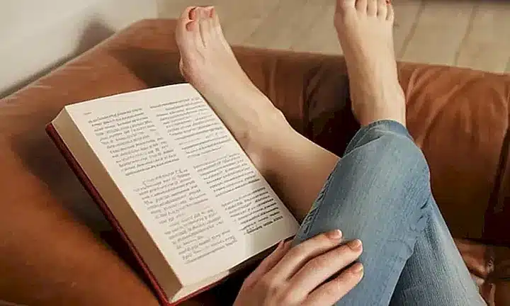 La habitación está tranquilamente iluminada por una luz que cae desde la ventana mientras el ocupante está profundamente inmerso en su lectura