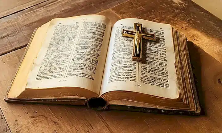Un antiguo libro de biblia se abre sobre una mesa de madera desgastada, iluminado suavemente por la luz matutina