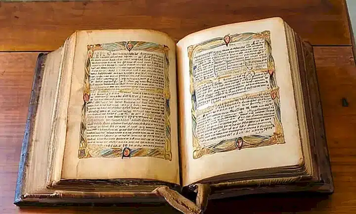 Una Biblia desgastada y encuadernada en cuero está abierta sobre una mesa de madera iluminada suavemente por la luz del sol