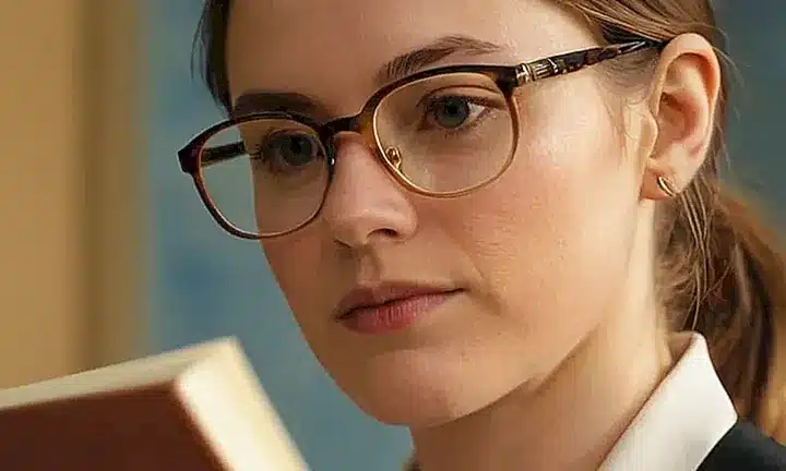 Una persona reflexiva con gafas y cabello grisono sentada junto a un viejo cuaderno lleno de notas, iluminado por una suave luz dorada