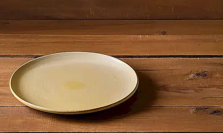 Un plato de cerámica en color beis con un toque amarillento se encuentra sobre una mesa de madera desgastada