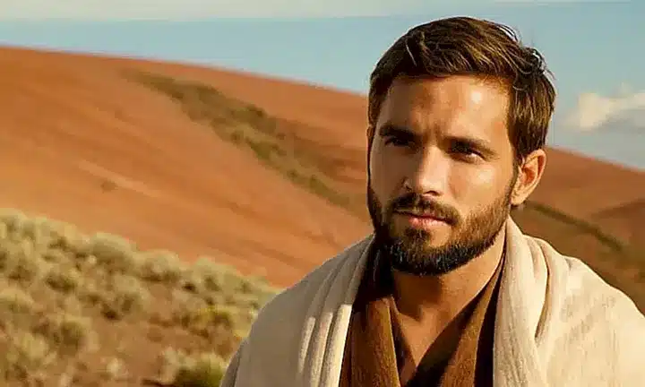Una imagen que describe un paisaje natural con un hombre barbudo y un joven sentados juntos cerca de una colina bajo el sol brillante