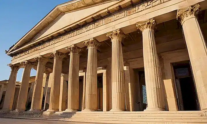 La fachada del edificio neoclásico presenta arcas monumentales con columnas dóricas, carretería y detalles delicados bañados en luz dorada