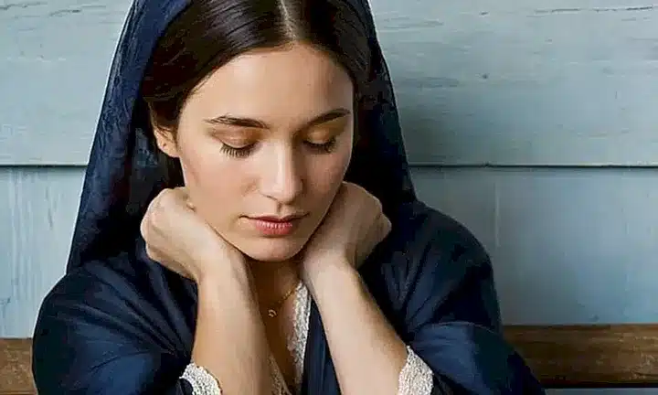 Maria sentada humildemente en un banco de madera, con su Biblia y un halo de calma envolviéndola