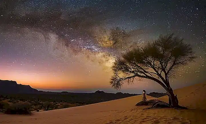 La estrella de Navidad brillante y plateada llena el cielo nocturno con una luz etérea, iluminando la llanura desértica y enfatizando las texturas de los antiguos rocas
