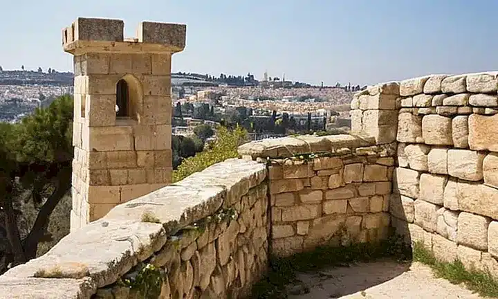 Un muro de piedra se eleva en una colina con vistas a la antigua ciudad de Jerusalén, cubierto por lichens y musgos