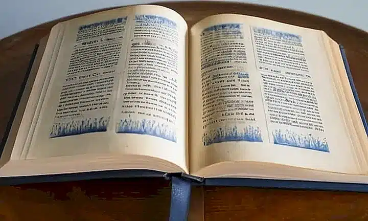 Una Biblia con cubierta dorada y letras emborronadas se abre ante una ventana bañada de luz natural que ilumina sus páginas