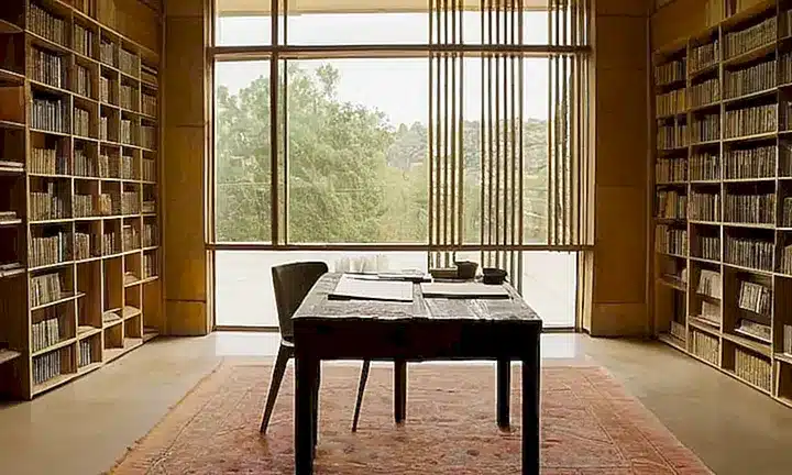 Dos personas trabajarían juntas en una habitación acogedora y tranquila, rodeadas de libros antiguos y materiales artísticos, iluminados por la suave luz natural que entra a través de las ventanas